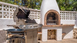 An outdoor cooking area with a grill and a brick oven, surrounded by a white wall with decorative lattice.