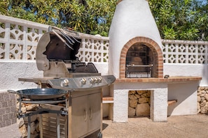 An outdoor cooking area with a grill and a brick oven, surrounded by a white wall with decorative lattice.