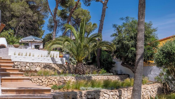 A stone staircase leading up to a white building with a tiled roof, surrounded by lush greenery and palm trees.