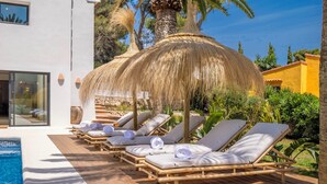 A poolside area with lounge chairs and a thatched umbrella.