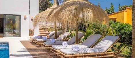A poolside area with lounge chairs and a thatched umbrella.