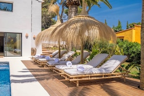 A poolside area with lounge chairs and a thatched umbrella.