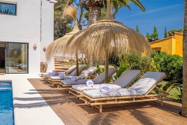 A poolside area with lounge chairs and a thatched umbrella.