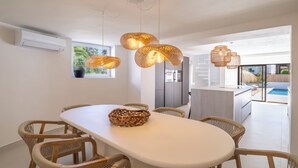 A modern dining area with a white table, wicker chairs, and woven pendant lights.