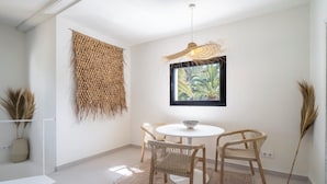 A minimalist dining area with a round table, two chairs, a woven wall hanging, and a framed picture of a plant.
