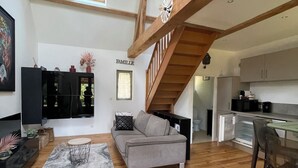 A spacious living area with a wooden staircase, a grey sofa, and a kitchen in the background.