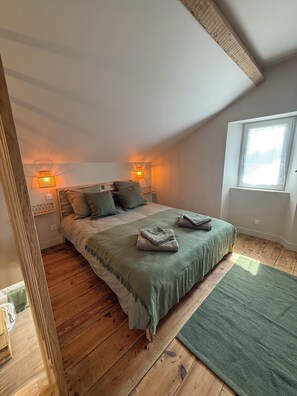 Ein Schlafzimmer mit Holzboden, einem Bett mit grüner Bettdecke, zwei Nachttischlampen und einem Fenster mit Aussicht.