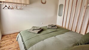 Um quarto com piso de madeira, uma cama com roupa de cama verde, um guarda-roupa de madeira e um varal fixado na parede.