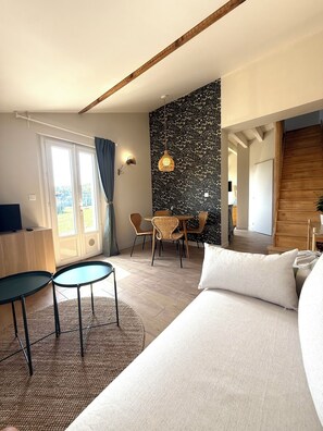Ein modernes Hotelzimmer mit einem großen Bett, einem Essbereich mit Korbstühlen, einem kleinen Tisch und Blick ins Freie durch eine Schiebetür.