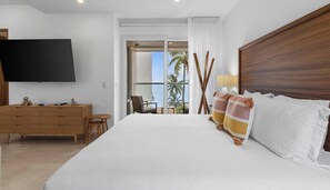 Una habitación de hotel con una cama grande, un televisor montado en la pared, un aparador de madera y un balcón con vista al océano.