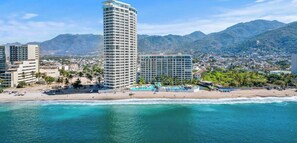 A coastal cityscape with a tall hotel, beach, and mountains in the background.