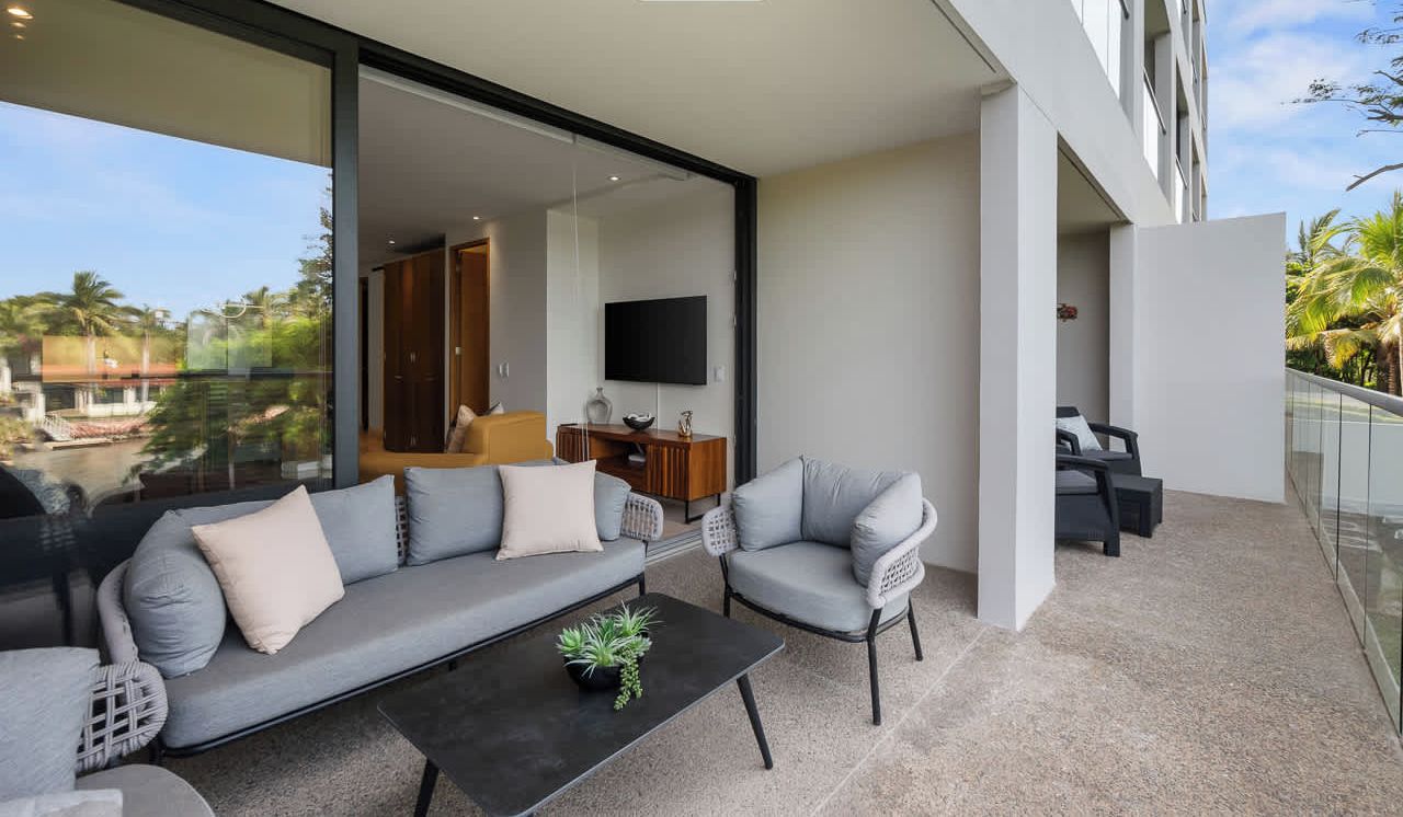 Un espacio moderno al aire libre con un sofá y sillones, una mesa baja y un televisor al fondo.