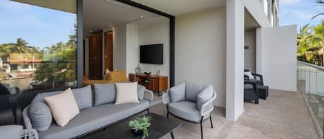 Un espacio moderno al aire libre con un sofá y sillones, una mesa baja y un televisor al fondo.