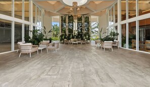 A spacious indoor area with wicker furniture, large windows, and a central chandelier.