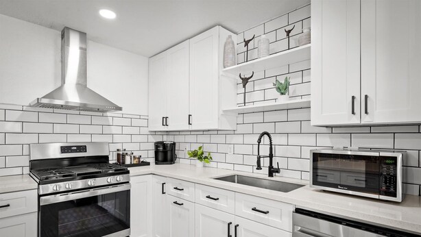 Een moderne keuken met witte kastjes, een roestvrijstalen afzuigkap, een inbouwoven, een magnetron en een vaatwasser.