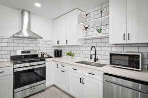 Una cocina moderna con armarios blancos, una campana extractora de acero inoxidable, horno integrado, microondas y lavavajillas.