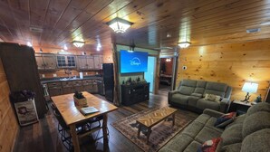 Un intérieur de chalet chaleureux avec des planchers en bois, un coin repas avec une table et des chaises, et un salon avec un canapé et un téléviseur diffusant Disney+.