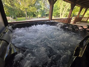 A hot tub with water bubbling, surrounded by a wooden deck and trees. - Country Cabin - Hot Tub - Free Kayaks - Gig Speed Internet - Fire Pit! (Loogootee)