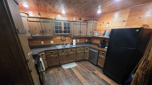 Une cuisine de style rustique, avec des meubles en bois, un réfrigérateur noir et un évier.