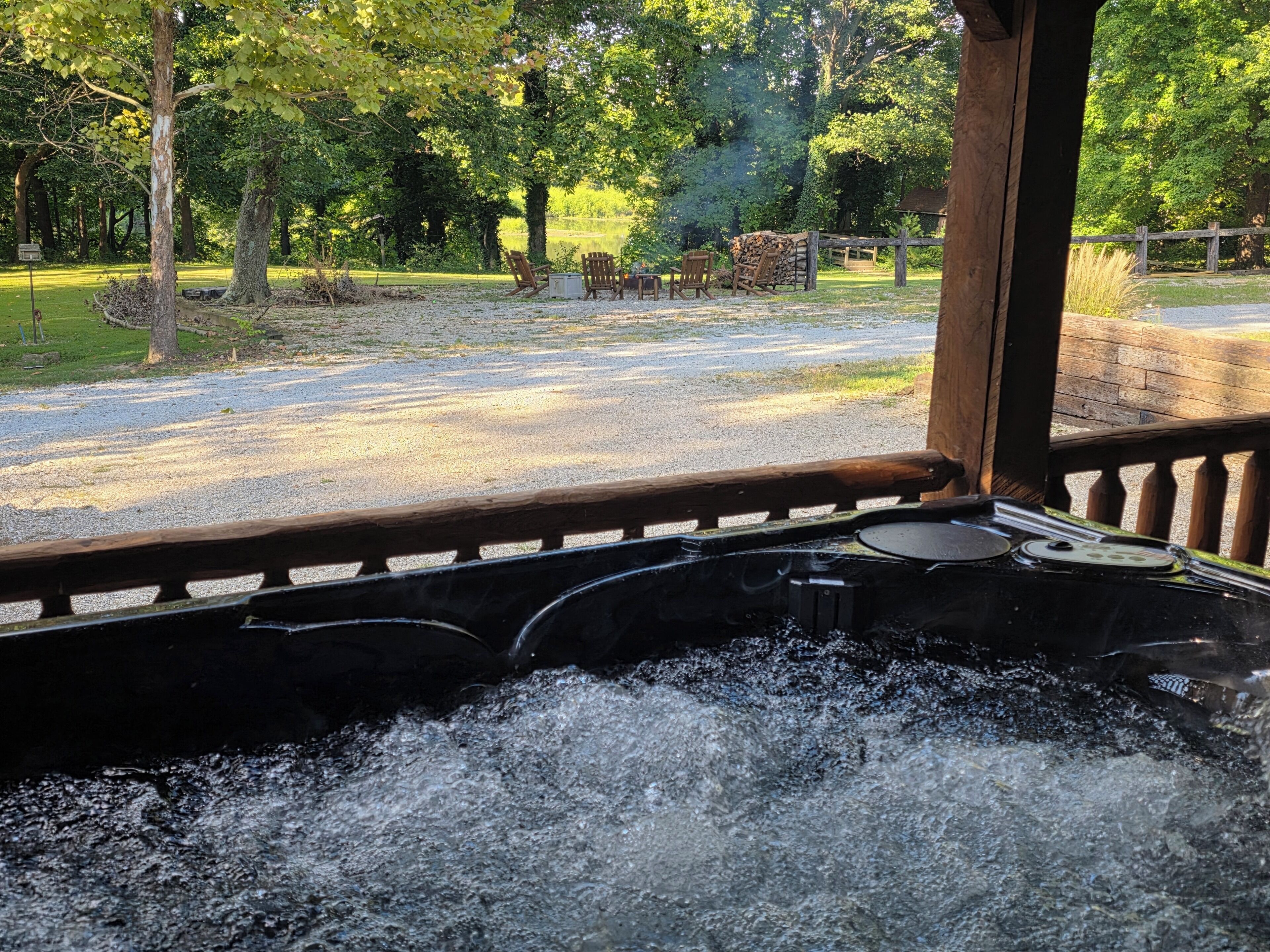 A hot tub with a wooden deck and a view of a park with trees and a gravel path.