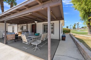 A covered patio with a dining table and chairs, a kitchen area, and a view of a golf course. - Portola Country Club, Golf, Pool, Pickleball (Palm Desert)