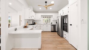 A modern kitchen with white cabinetry, a central island, a built-in oven, and a ceiling fan.