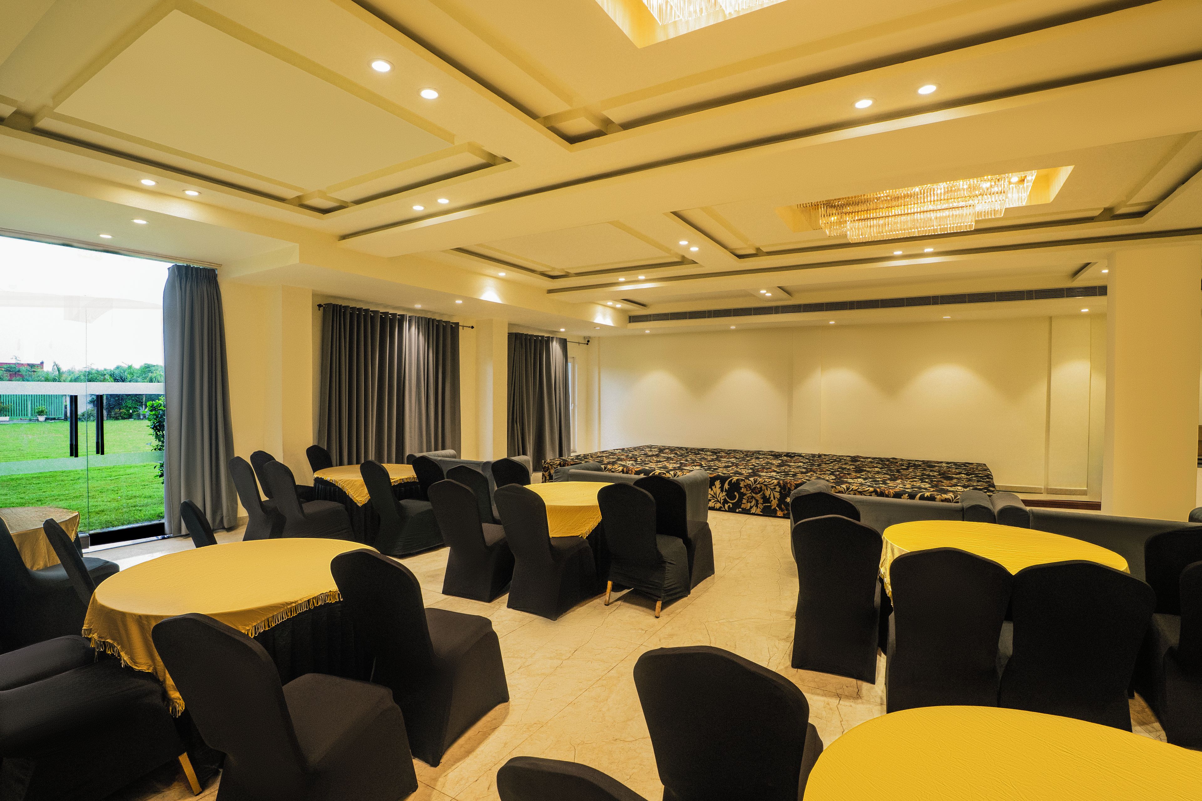 A conference room with multiple tables and chairs, a large screen, and a view of a green landscape through the windows.
