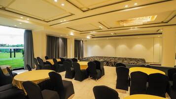 A conference room with multiple tables and chairs, a large screen, and a view of a green landscape through the windows.