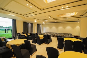 A conference room with multiple tables and chairs, a large screen, and a view of a green landscape through the windows. - Savanna Retreat by Nuva Stayz (Ramnagar)