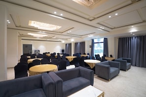 Un salón de conferencias con mesas redondas, sillas y sofás, equipado con iluminación en el techo y un amplio ventanal.