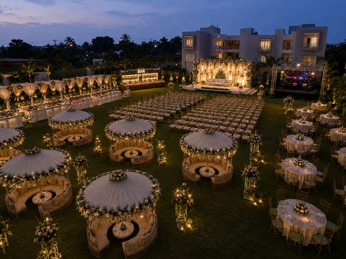 Espaço para eventos ao ar livre com mesas redondas, áreas de estar, bar e palco com iluminação.