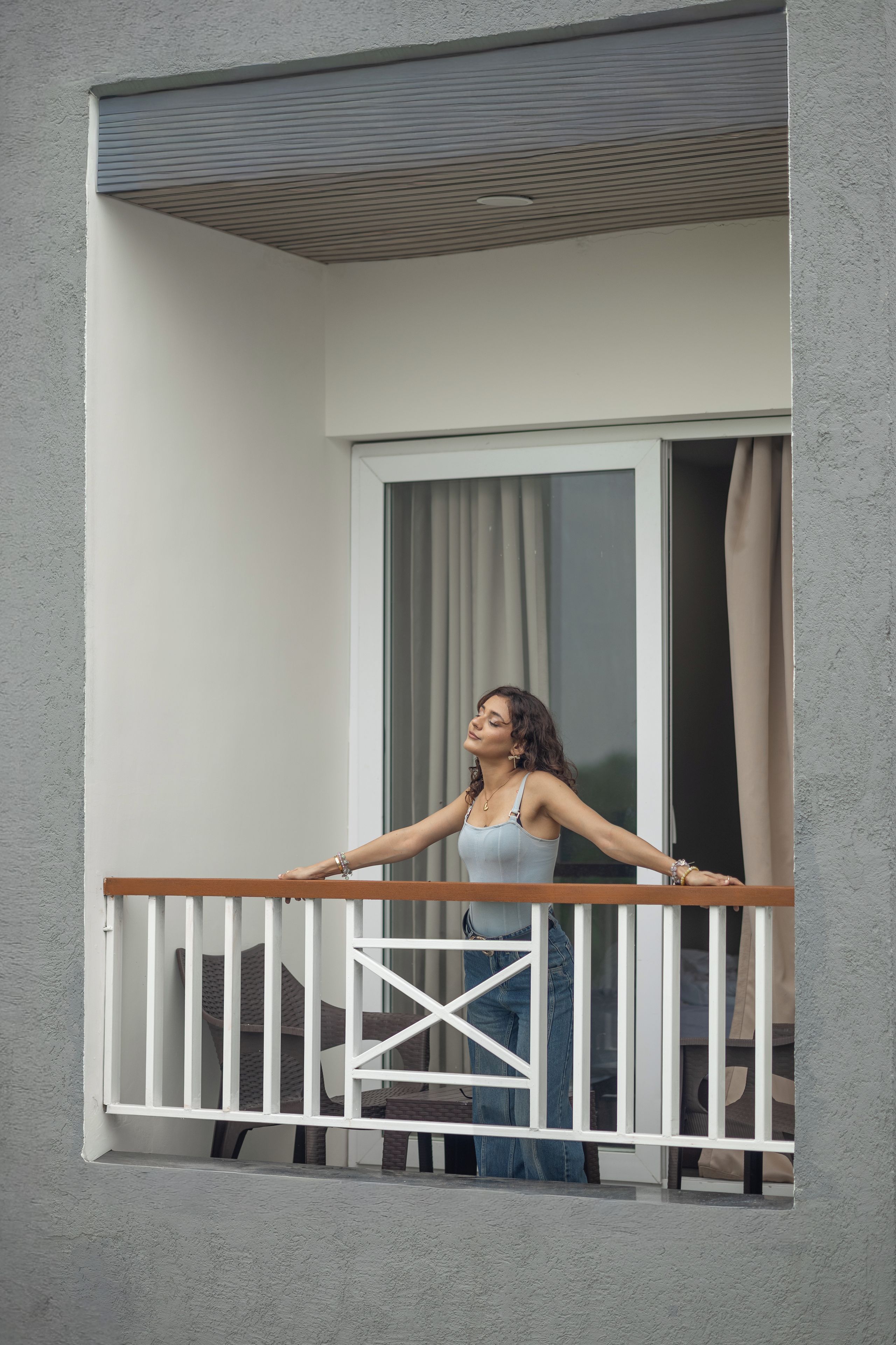 Un balcó amb barana de fusta, una finestra amb cortines i vista a l'exterior.