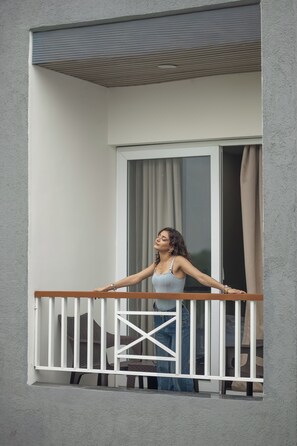 A balcony with a wooden railing, a window with curtains, and a view of the outside. - Savanna Retreat by Nuva Stayz (Ramnagar)