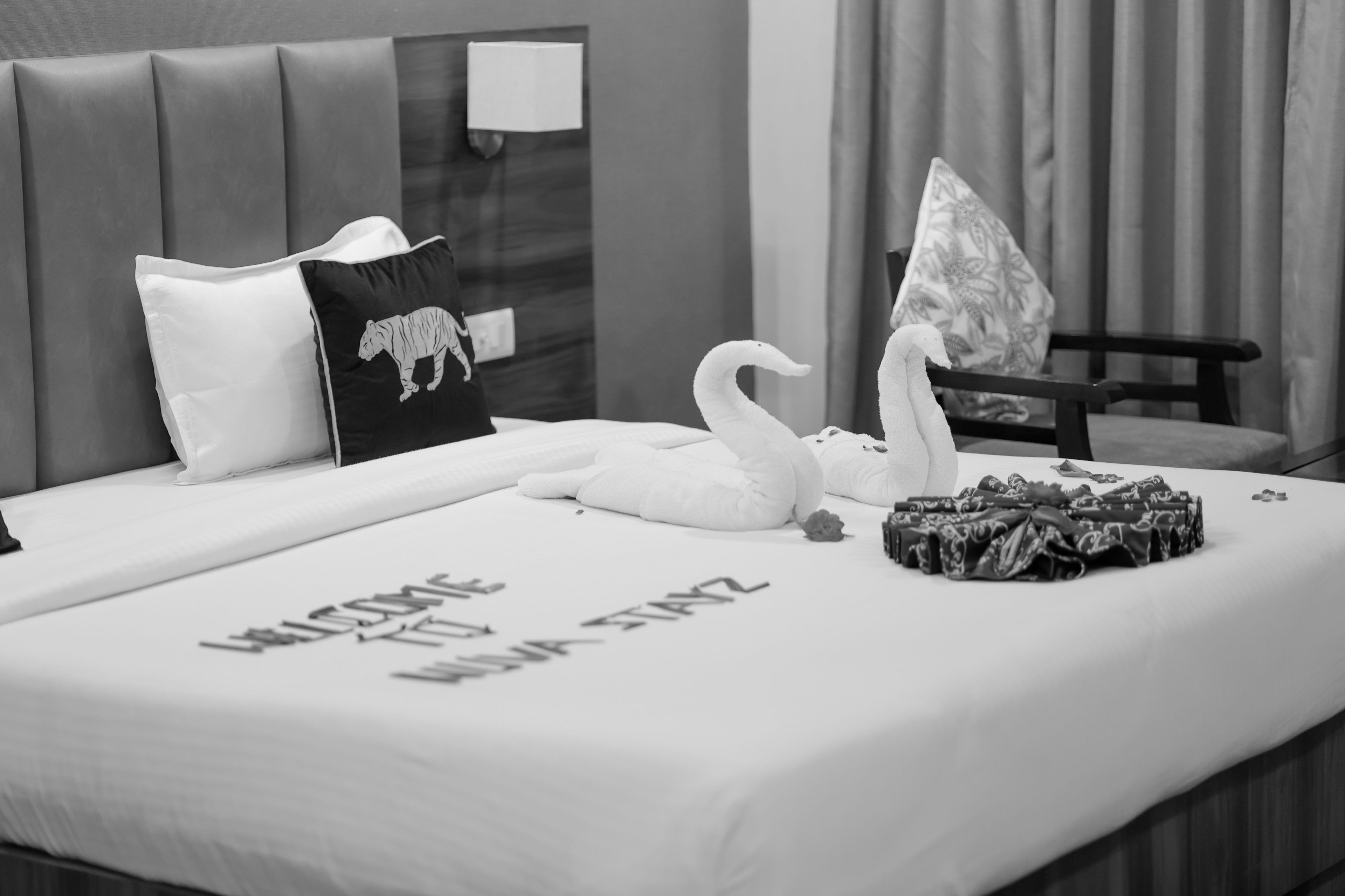 Habitación de hotel con cama, almohadas, una decoración de cisne y un cartel de bienvenida.