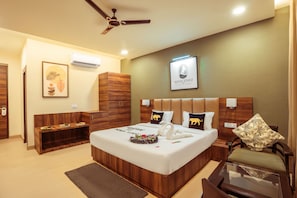 Una habitación de hotel moderna con una cama grande, una mesita de noche, una silla, un ventilador de techo y un cartel de bienvenida enmarcado.