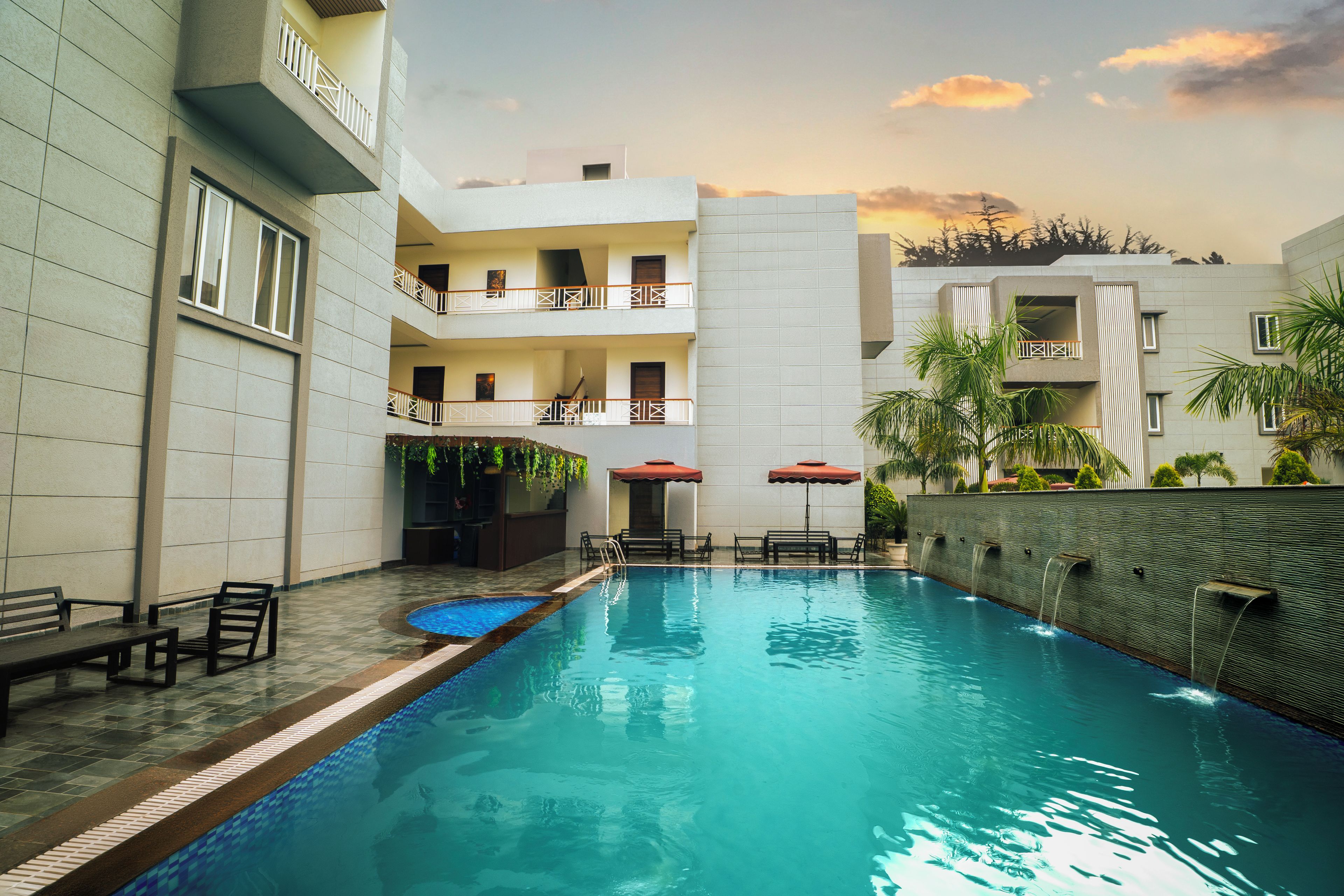 A swimming pool with a tiled deck, benches, and umbrellas.