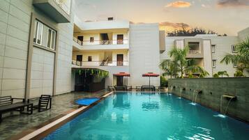 A swimming pool with a tiled deck, benches, and umbrellas.