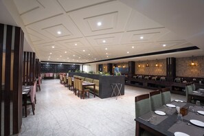 Un restaurante espacioso con una barra larga, varias mesas de comedor y un techo alto con iluminación empotrada.