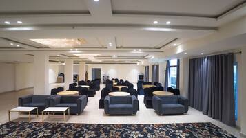 A spacious conference room with rows of chairs and tables, a patterned carpet, and a modern ceiling design.