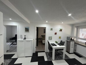 A modern, well-lit room with a dining area, a kitchenette, and a bed.