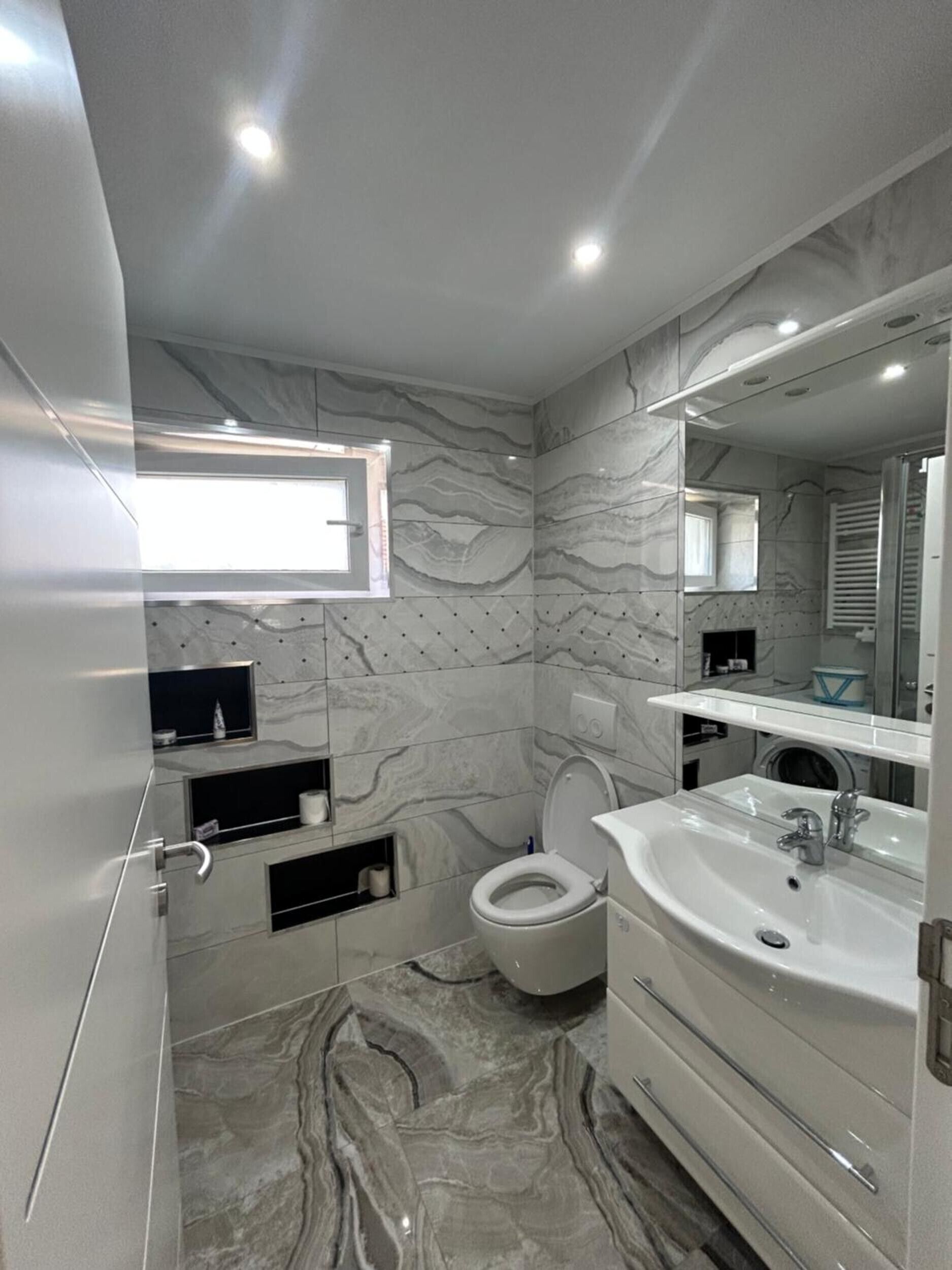 A modern bathroom with a marble floor, a white sink, and a toilet.
