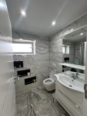 Une salle de bain moderne avec un sol en marbre, un lavabo blanc et des toilettes.