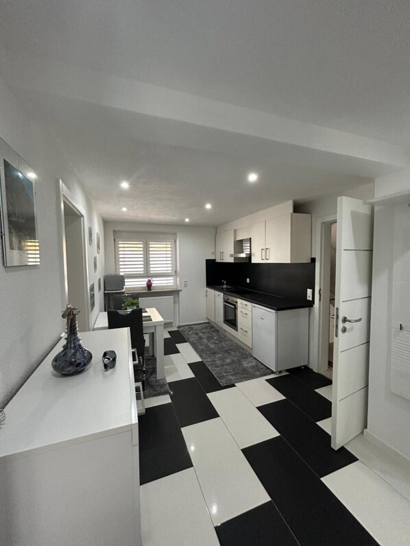 A modern kitchen with white cabinets, a black countertop, and a checkered floor.