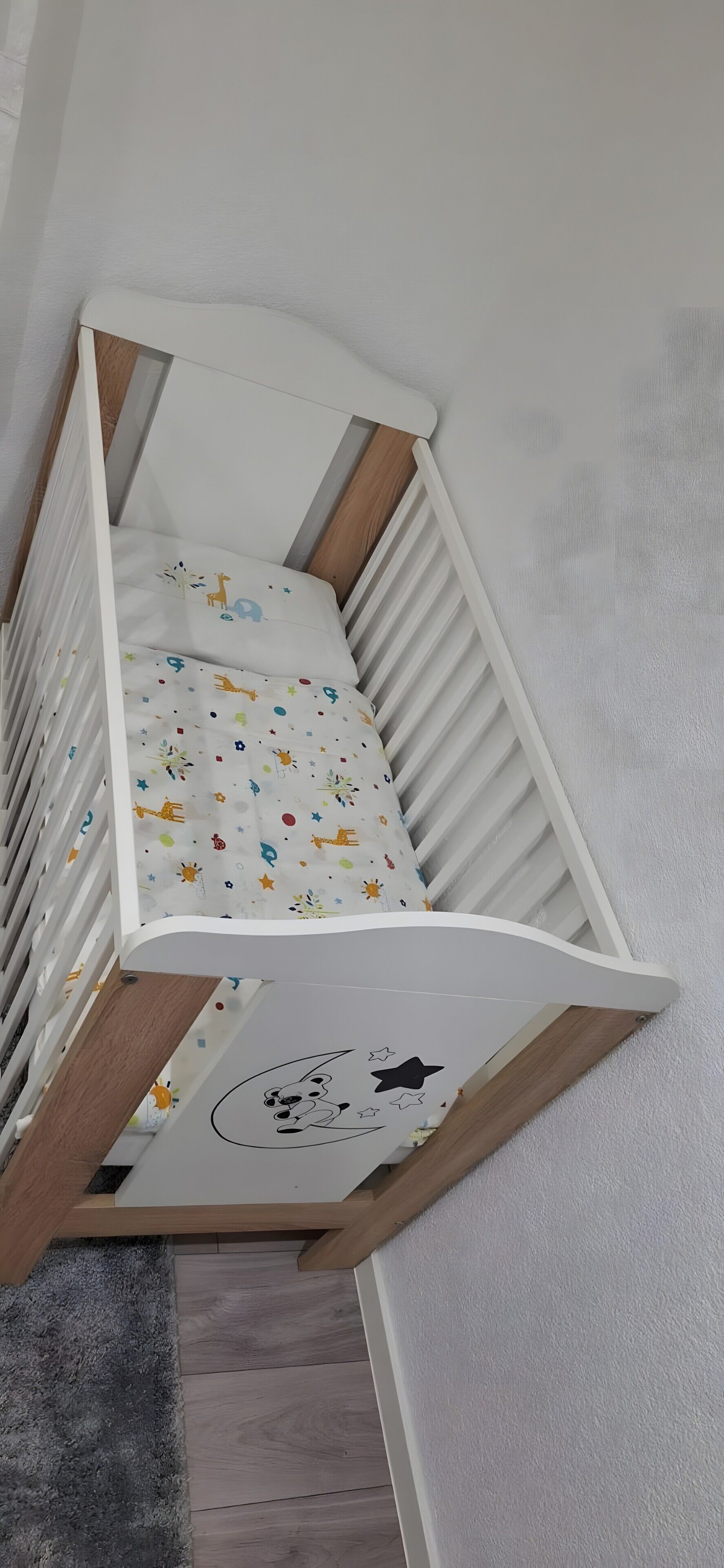 Un berceau blanc avec un matelas coloré à motifs, placé contre un mur blanc, le tout sur un plancher en bois.