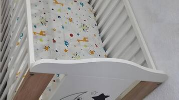 A white crib with a colorful patterned mattress, positioned against a white wall with a wooden floor.