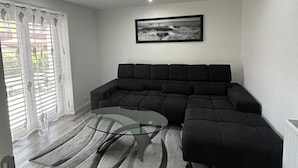 Een moderne woonkamer met een hoekbank, een glazen salontafel en een ingelijst schilderij aan de muur.