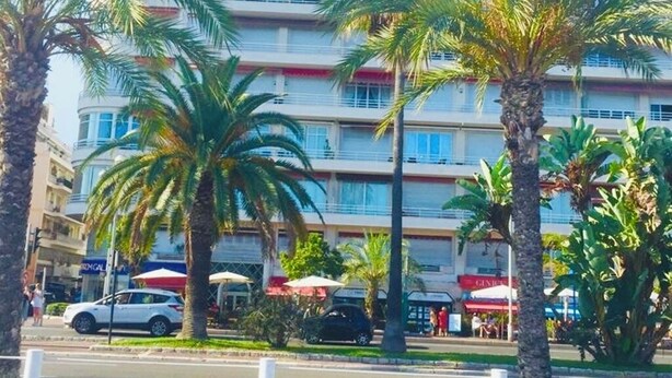 A multi-story hotel with balconies, palm trees, and outdoor seating areas.