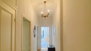 A narrow hallway with wooden flooring, a chandelier, and a bench.
