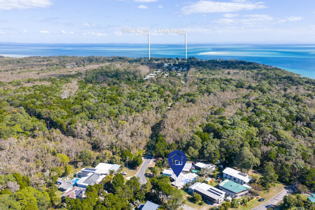 An aerial view of a resort with a dense forest surrounding it, a road leading to the buildings, and a clear view of the ocean.