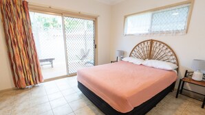 Een slaapkamer met een bed, een raam, een stoel en een nachtkastje.